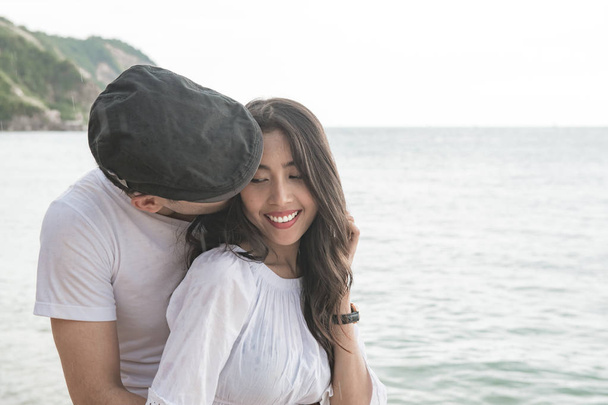 Couple holding each other on beach. Young happy interracial couple on beach holding each other. Asian woman, Caucasian man. Young mixed race romance concept. - Fotografie, Obrázek