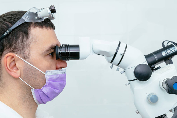 Dentist looking through a microscope in a modern clinic - Фото, изображение