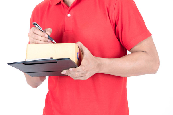 Young logistic career concept. Happy delivery man with box and taking notes. Isolated on white background. Asian chinese fit man in red polo shirt and jeans with red hat in his early twenties. - Fotó, kép