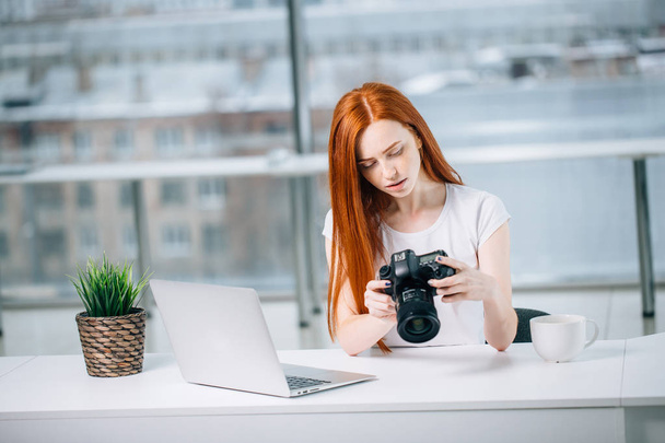 redhead woman looking at camera while working on laptop - Φωτογραφία, εικόνα