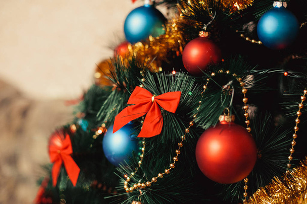 Close-up kerstboom ornamenten gemaakt van glas met gekleurde rode, blauwe ballen, gouden klatergoud, red strikken, gouden tekenreeksen kralen met glitter en warme verlichting detail. Nieuwjaar en concept vakantie 2018. - Foto, afbeelding