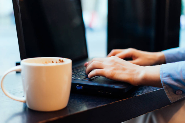 女の子がコーヒー カップの横にノート パソコンのキーボードをクリックすると - 写真・画像