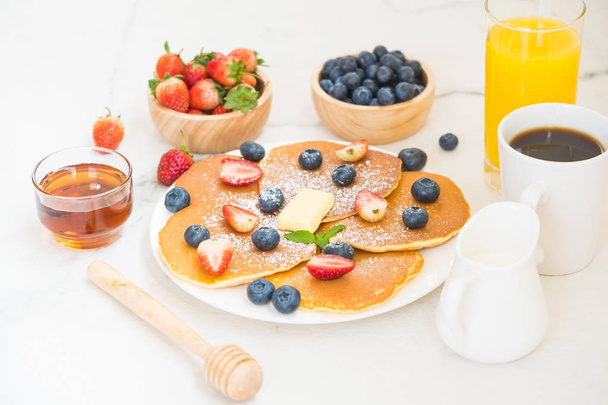 Healthy Breakfast set with Pancake blueberry and strawberry fruits and black coffee , Milk and Orange juice on white stone table background - Photo, Image