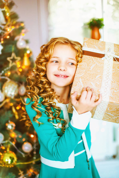 Little girl with long curly hair at home at christmas tree with gifts - Photo, image