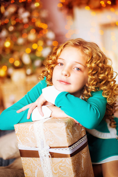 Little girl with long curly hair at home at christmas tree with gifts - Foto, Imagem