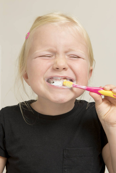 Sorridente bambina in camicia nera spazzolando i denti
 - Foto, immagini