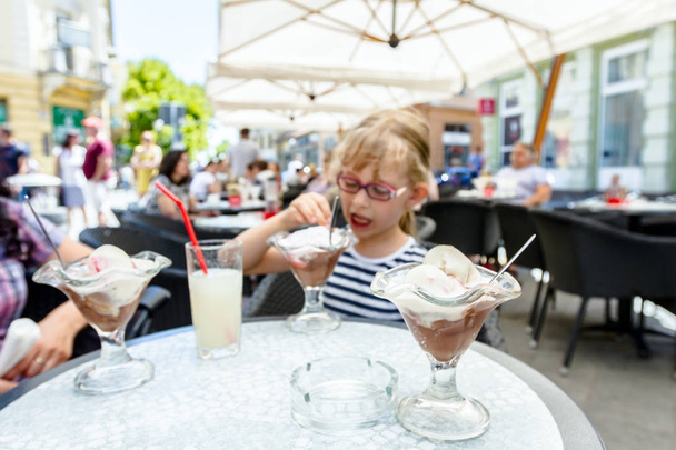 Süßes kleines Mädchen mit Brille isst Eis im Restaurant - Foto, Bild