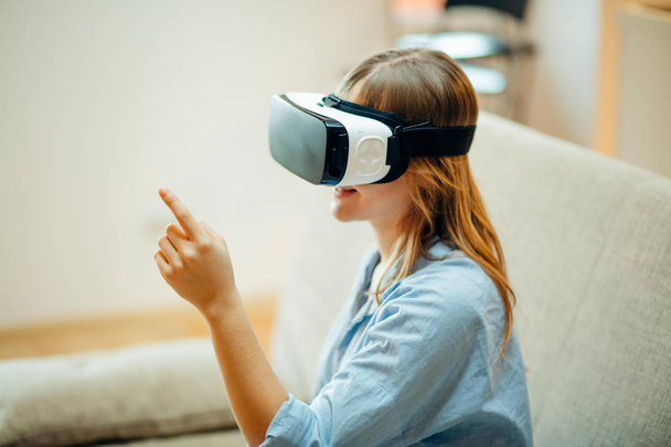 woman adjusting her VR headset and smiling while sitting on the carpet at home - Фото, изображение