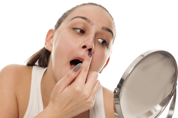 Молодая женщина проверяет волосы в носу в зеркале
 - Фото, изображение