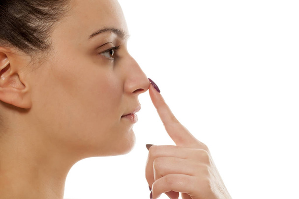 Mujer joven tocándose la nariz sobre un fondo blanco
 - Foto, Imagen
