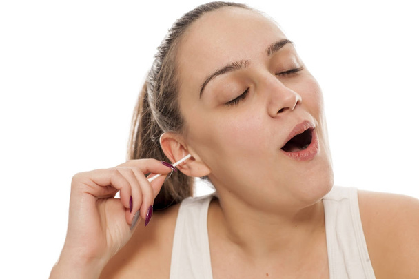 Молодая женщина наслаждается чисткой уха ватным тампоном
 - Фото, изображение