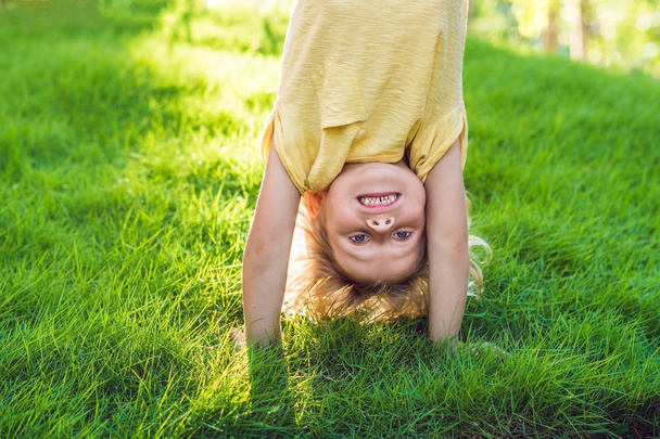 Portrait of happy kid playing upside down outdoors in summer park walking on hands - Foto, Imagen