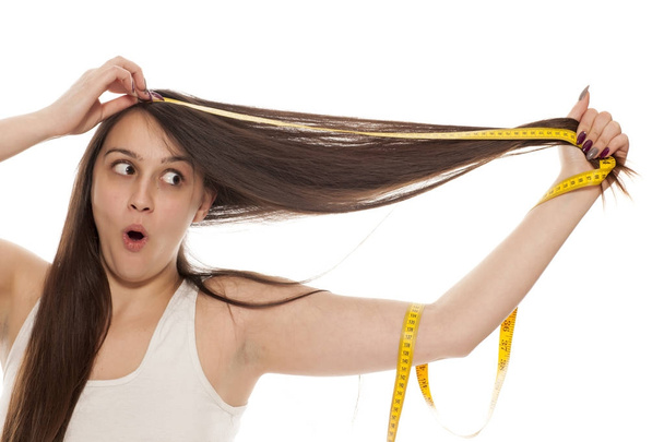 Jovem mulher abandonada segurando fita métrica e mostrando o comprimento de seu cabelo
 - Foto, Imagem