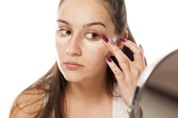 Jeune femme appliquant un correcteur sous ses yeux avec ses doigts
 - Photo, image