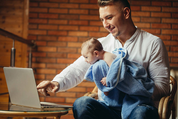 Pai com bebê recém-nascido trabalhando a partir de casa usando laptop
 - Foto, Imagem