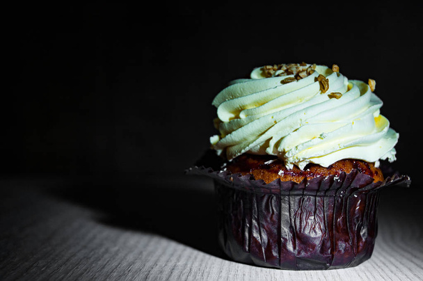 Yummy cupcake with buttercream on wooden table against dark background with copy space. - Foto, afbeelding