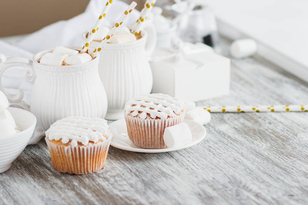 Cups with cacao and marshmallow, cupcakes and different decorations, wooden background - Photo, Image