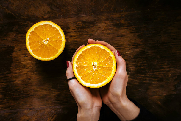 A girl holding a half of orange on a wooden table - Photo, image