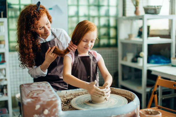 redhead mother and her child daughter moulding with clay on pottery wheel - Foto, Imagen