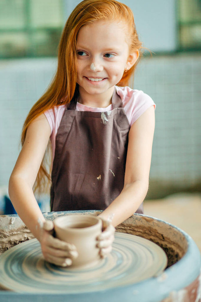 redhead Child sculpts from clay pot. workshop on modeling on potters wheel. - Zdjęcie, obraz