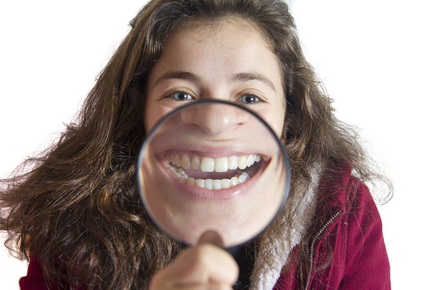 Girl smiling and show teeth through a magnifying glass over white background - Photo, Image