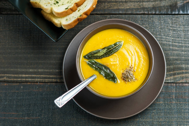 pumpkin soup with sage leaves in brown ceramic soup plate with garlic bread. - 写真・画像