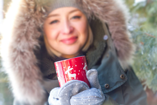 Téli lány portré meleg szőrme sapka zöld háttér piros pohár a kezében - Fotó, kép