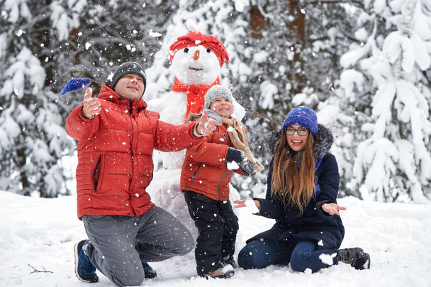 Diversión invernal. una chica, un hombre y un niño haciendo un muñeco de nieve
. - Foto, imagen