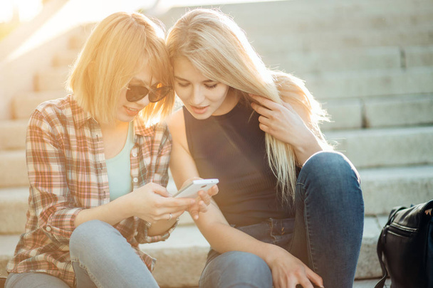 Two beautiful students watching media content on line in smart phone in park - Foto, Imagem