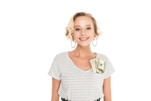beautiful young woman with dollar banknotes in pocket of t-shirt smiling at camera isolated on white - Photo, Image