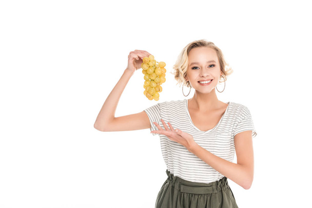 beautiful young woman holding bunch of fresh ripe grapes and smiling at camera isolated on white - Photo, Image