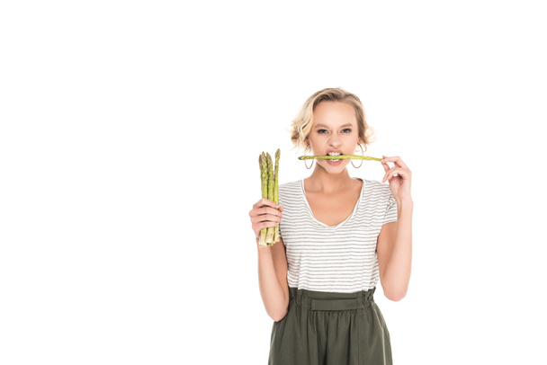Portret van de jonge vrouw bijten rauwe asperges in handen geïsoleerd op wit - Foto, afbeelding