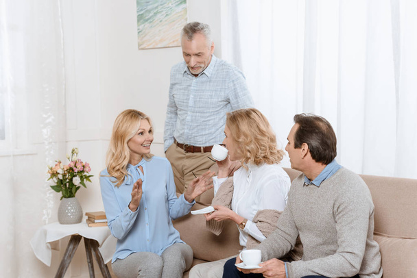 Старші чоловіки і жінки розмовляють під час пиття чаю на дивані
 - Фото, зображення