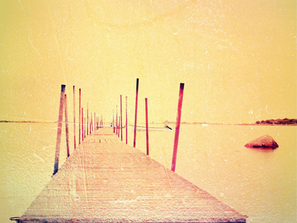 Abstract effect. Wet wooden pier in smooth water of sea bay.  Old mole anchored with steel poles - Photo, Image