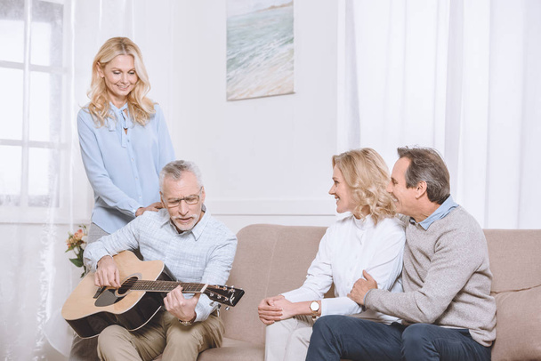 Чоловіки та жінки середнього віку слухають гітарну музику у вітальні
 - Фото, зображення