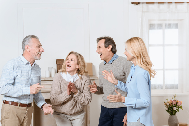 Senior men and women having friendly conversation and laughing in living room - Photo, Image