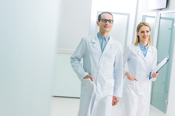 smiling doctors in white coats with diagnosis in hospital corridor - Фото, изображение