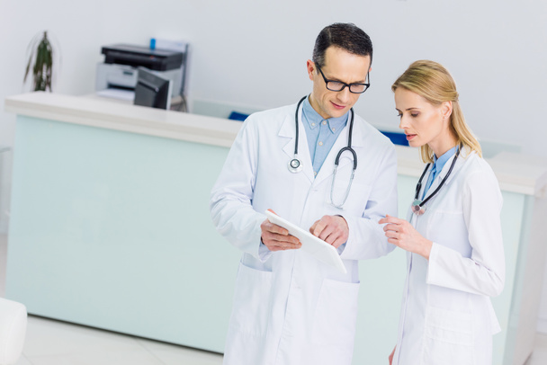kaksi lääkäriä valkoisissa takeissa tabletin kanssa keskustelevat diagnoosista klinikalla
 - Valokuva, kuva