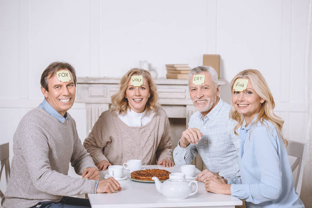 friends playing card game with words on foreheads while sitting at table   - Photo, Image