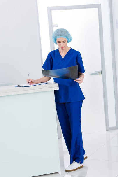female surgeon looking at x-ray and writing diagnosis in clinic - Foto, Bild