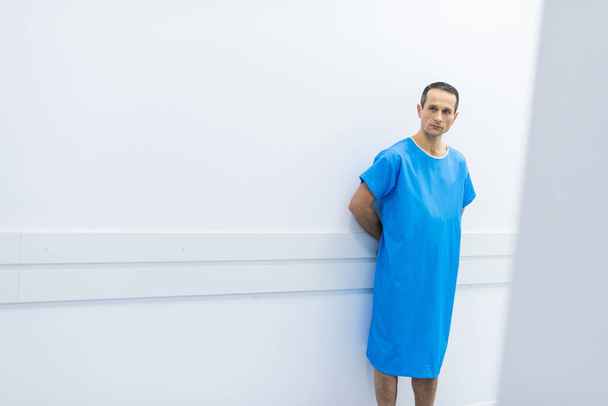 patient homme en robe médicale debout au mur à l'hôpital
  - Photo, image