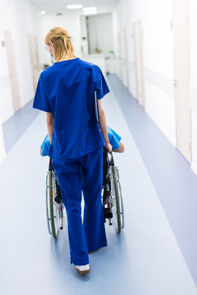 rear view of surgeon and upset patient in wheelchair in hospital corridor  - Foto, Imagen