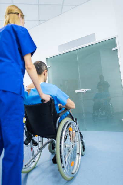 back view of surgeon and male patient in wheelchair in hospital corridor  - 写真・画像