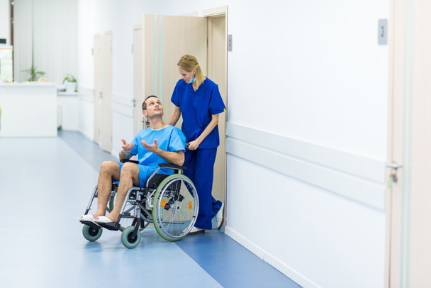 surgeon talking with male patient in wheelchair in hospital corridor  - Foto, afbeelding