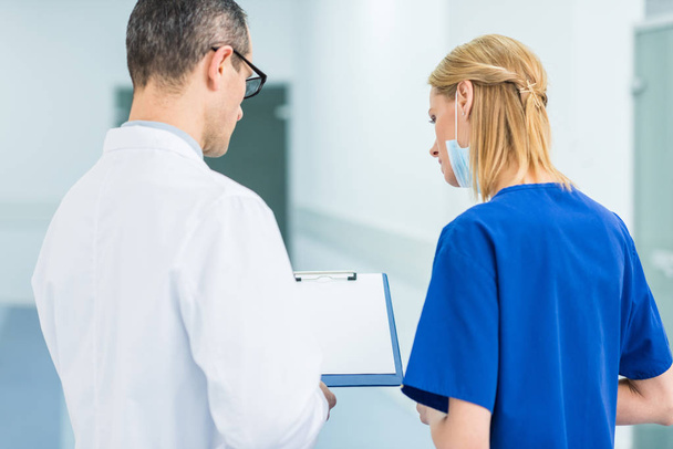 vista posterior del médico en bata blanca y cirujana mujer discutiendo el diagnóstico en el hospital
 - Foto, Imagen