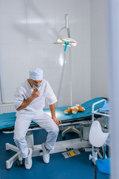 zdenerwowany lekarz siedzi na medycznych łóżko, leżącego w pobliżu Pluszak - Zdjęcie, obraz