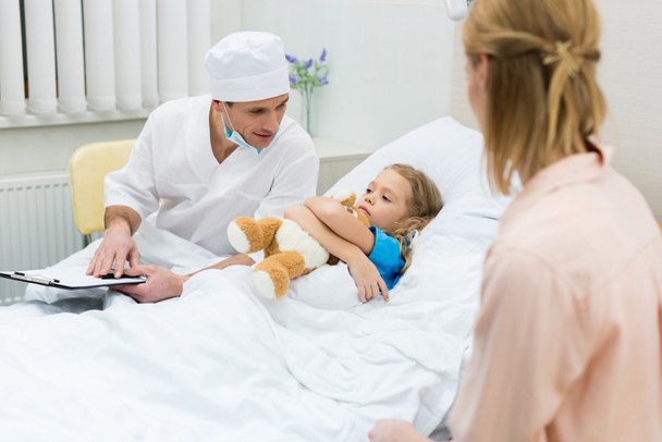 doctor sitting with clipboard and talking with kid patient - Photo, image