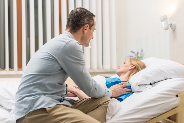 Mann sitzt am Krankenbett seiner Frau im Krankenhaus - Foto, Bild