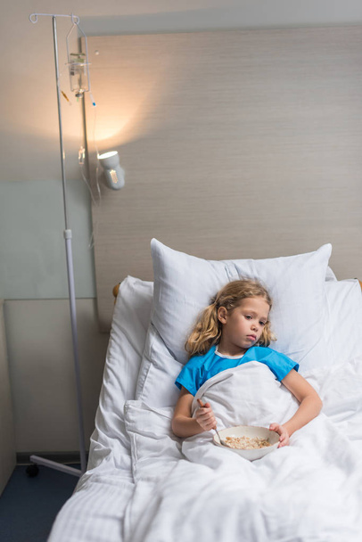 preschooler kid lying on bed in hospital with plate of oatmeal  - Foto, imagen