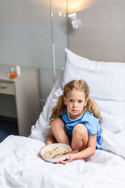 preschooler kid sitting on bed in hospital with plate of oatmeal  - Photo, Image